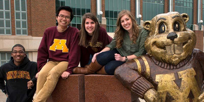 group of students wearing maroon and gold next to bronze Goldy Gopher statue